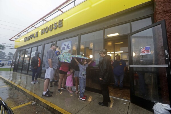 FILE - Luke Churchill, left, stands with his wife, Mary and their children, Katie, 13, Liam, 9, and Raighan, 3, as they wait in the rain outside an open Waffle House restaurant in Wilmington, N.C., after Hurricane Florence traveled through the area, Sept. 16, 2018. (AP Photo/Chuck Burton, File)