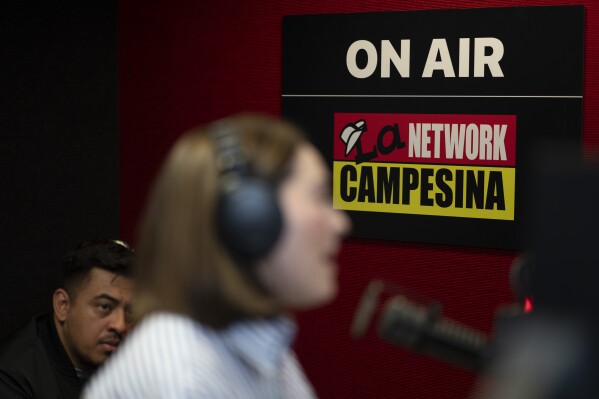 As Michael Ruiz, left, looks on, radio guest Carolina Rodriguez-Greer, with Mi Familia Vota, speaks, at the Phoenix studio of La Campesina, a Spanish-language radio network, Wednesday, March 20, 2024. A surge of misinformation is targeting Spanish-speaking voters with a high-stakes presidential election looming in the fall and candidates vying for support from the rapidly growing number of Latino voters. In one of the most important swing states, Arizona, La Campesina is countering that with a dedicated effort to provide Latino voters the facts about voting and how elections are run. (AP Photo/Serkan Gurbuz)