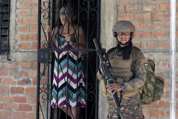 A resident looks out from her doorway as a soldier takes part in an operation in search of gang members, in Soyapango, El Salvador, Saturday, Dec. 3, 2022. The government of El Salvador sent 10,000 soldiers and police to seal off Soyapango, on the outskirts of the nation’s capital Saturday. (AP Photo/Salvador Melendez)
