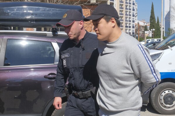 FILE - Montenegrin police officers escort South Korean citizen, Terraform Labs founder Do Kwon in Montenegro's capital Podgorica, March 24, 2023. A court in Montenegro has ruled that Do Kwon should be extradited to the United States to face fraud charges rather than to his native South Korea, a court official in the Balkan Country said Thursday Feb. 22, 2024. Do Kwon, 32, was arrested nearly a year ago in Montenegro on an international arrest warrant in connection with a $40 billion crash of Terraform Labs' cryptocurrency, which devastated retail investors around the world. (APPhoto/Risto Bozovic, File)