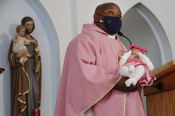 The Rev. Athanasius Abanulo introduces newborn, Nathalia Perez, to the congregation at Immaculate Conception Catholic Church on Sunday, Dec. 12, 2021, in Wedowee, Ala. Originally from Nigeria, Abanulo is one of numerous international clergy helping ease a U.S. priest shortage by serving in Catholic dioceses across the country. (AP Photo/Jessie Wardarski)