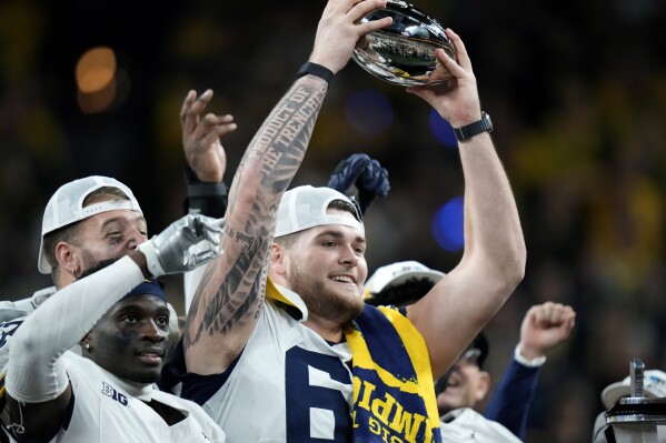 FILE - Michigan offensive lineman Zak Zinter (65) holds the trophy after the Big Ten championship NCAA college football game against Iowa, Saturday, Dec. 2, 2023, in Indianapolis. The lure of starting a pro career apparently isn’t quite as tempting for underclassmen now as it was in the days before college stars could profit off their name, image and likeness. Zinter didn’t enter last year’s draft and instead stayed for his senior season and helped the Wolverines win a national title. (AP Photo/AJ Mast, File)