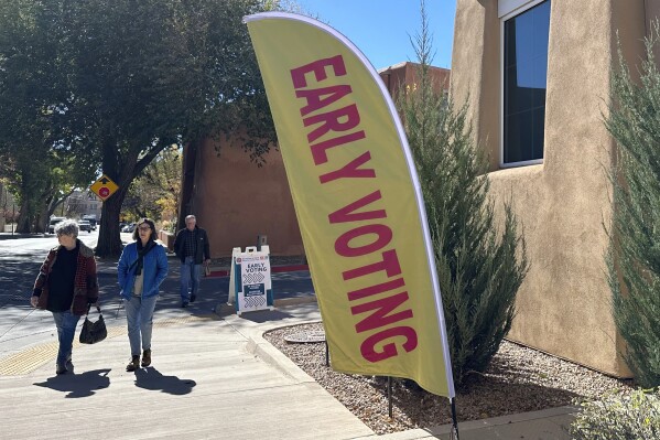 Pedestrians pass by a polling location in Santa Fe, N.M., on Thursday, Nov. 2, 2023. Voters are deciding whether to tax mansions to pay for affordable housing initiatives in a state capital city prized for its desert-mountain vistas, vibrant arts scene and stucco architecture rooted in Native American and Spanish-colonial tradition. (AP Photo/Morgan Lee)