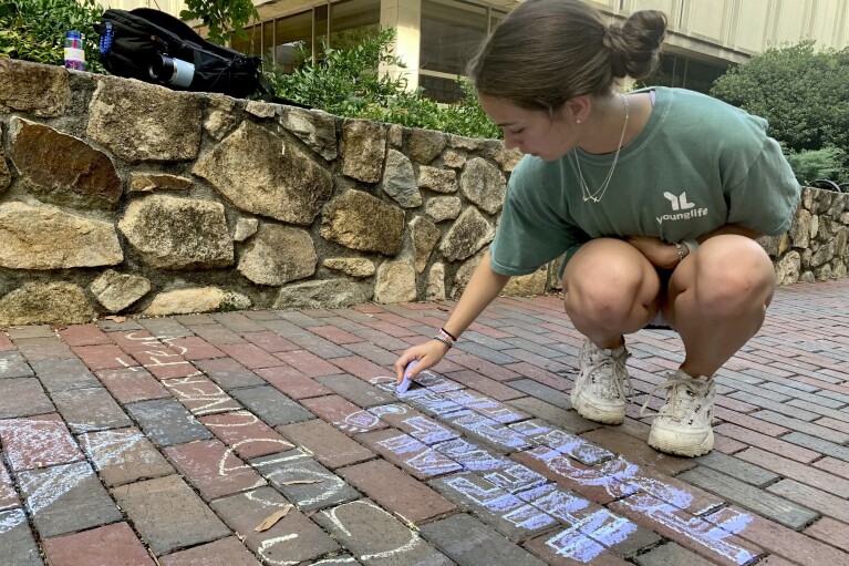 UNC-Chapel Hill sophomore Ashley Tatem writes "Heal Together" on a walking path outside the campus student center in Chapel Hill, N.C., Tuesday, Aug. 29, 2023, the day after a graduate student fatally shot his faculty adviser. (AP Photo/Hannah Schoenbaum)