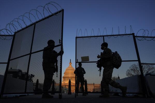 FILE - National Guard soldiers open a gate of the razor wire-topped perimeter fence around the Capitol to allow a colleague in at sunrise in Washington, March 8, 2021. (AP Photo/Carolyn Kaster, File)