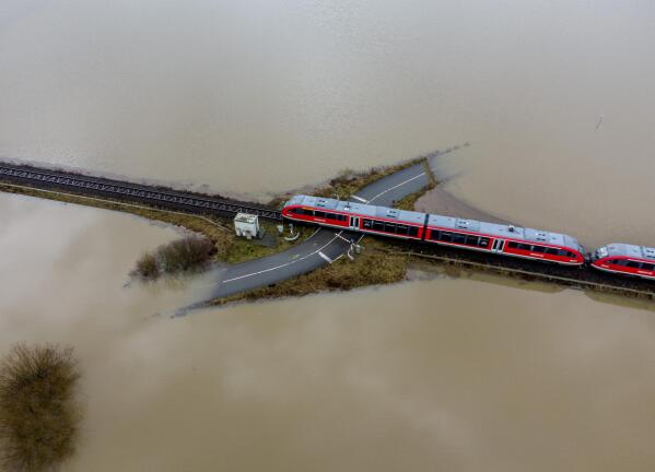 A train passes a railroad crossing surrounded by floodwaters from rain and melting snow in Nidderau near Frankfurt, Germany, Wednesday, Feb. 3, 2021. (AP Photo/Michael Probst)