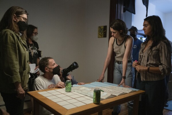 This image released by Focus Features shows writer/producer Tricia Cooke, left, director/writer/producer Ethan Coen, kneeling, actor Margaret Qualley, second right and actor Geraldine Viswanathan, right, on the set of "Drive-Away Dolls." (Wilson Webb/Focus Features via AP)