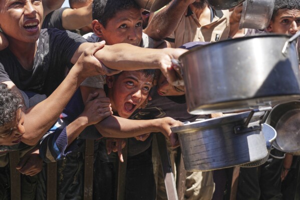 Palestinians struggle to receive cooked food distributed at a community kitchen in the Muwasi area of Khan Younis, in the Gaza Strip, Friday, May 23, 2025. (AP Photo/Abdel Kareem Hana)