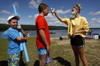 As a precaution to help prevent the spread of coronavirus, beach attendant Danielle McClure takes the temperature of Colten Ryan before allowing him and his brother, Finn, left, to enter Maranacook Beach, Wednesday, Aug. 5, 2020, in Winthrop, Maine. (AP Photo/Robert F. Bukaty)
