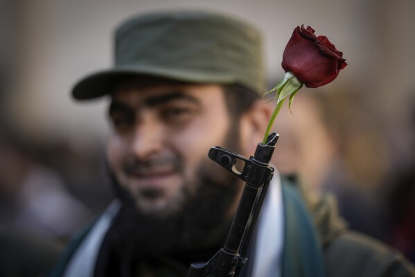 A Syrian fighter holds a gun with a flower placed in the barrel, as people gather for Friday prayers at the Umayyad mosque in Damascus, Syria, Friday, Dec. 13, 2024. (AP Photo/Leo Correa, File)
