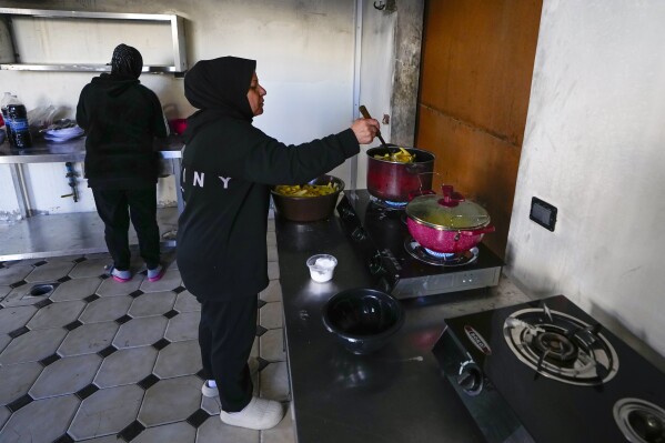 Mervat Reslan, right, cooks food for Iftar during the Muslim holy month of Ramadan at an abandoned hotel in Marwanieh, Lebanon, on Friday, March 15, 2024. (AP Photo/Bilal Hussein)