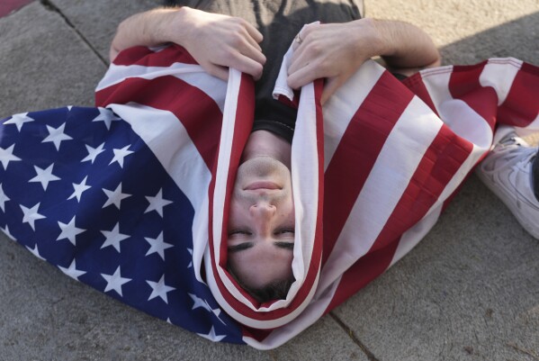 A demonstrator wraps themselves with a U.S. flag during a protest outside Dodger Stadium Saturday, June 21, 2025, in Los Angeles. (AP Photo/Damian Dovarganes)