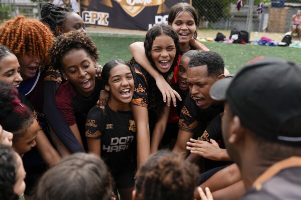 Young women and their coach Dioguinho bring it in for a team huddle at the start of a soccer training session run by the Bola de Ouro social program, at the Complexo da Alemao favela in Rio de Janeiro, Brazil, May 16, 2024. Young women are participating in soccer programs led by community trainers, where they receive both sports and personal development training. (AP Photo/Silvia Izquierdo)