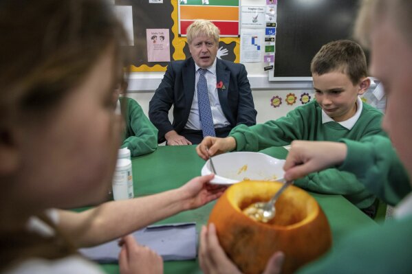 Britain's Prime Minister Boris Johnson sits with students as they carve pumpkins at Abbots Green Primary Academy in Bury St Edmunds, England, Thursday, Oct. 31, 2019. The opposition Labour Party kicked off its campaign for Britain's December general election with one overriding message Thursday: It's not just about Brexit. (Chris J Ratcliffe/Pool Photo via AP)