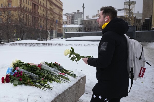 A man lays flowers paying the last respect to Alexei Navalny at the monument, a large boulder from the Solovetsky islands, where the first camp of the Gulag political prison system was established, with the historical the Federal Security Service (FSB, Soviet KGB successor) building in the background, in Moscow, Russia, on Saturday morning, Feb. 17, 2024. (AP Photo/Alexander Zemlianichenko)