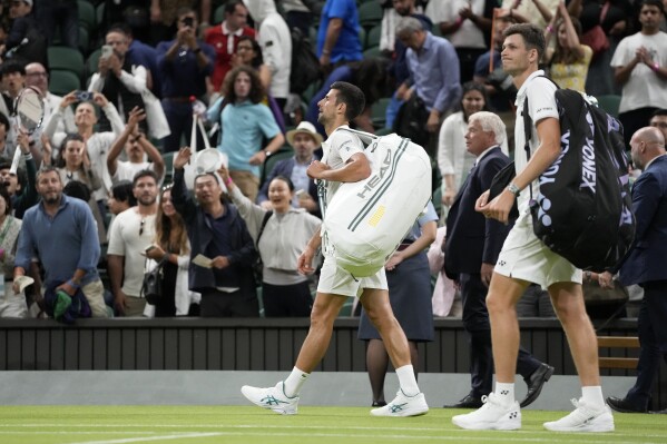 Serbia's Novak Djokovic, right, and Poland's Hubert Hurkacz leave the court after their men's singles match was suspended due to the lateness of the hour on day seven of the Wimbledon tennis championships in London, Sunday, July 9, 2023. (AP Photo/Kirsty Wigglesworth)