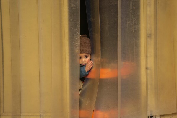 A toddler peeks out of a plastic curtain on a cold day in Srinagar, Indian controlled Kashmir, Thursday, Nov 23, 2023. (AP Photo/Mukhtar Khan)