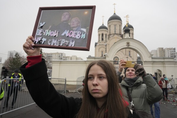 A woman holds a portrait of Alexei Navalny, left, and his wife Yulia, signed 