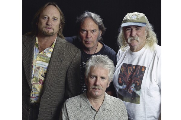 Musicians Stephen Stills, left, Neil Young, background center, Graham Nash, seated, and David Crosby pose for a photo at the Pierre Hotel, Oct. 13, 1999, in New York. (AP Photo/Jim Cooper, File)