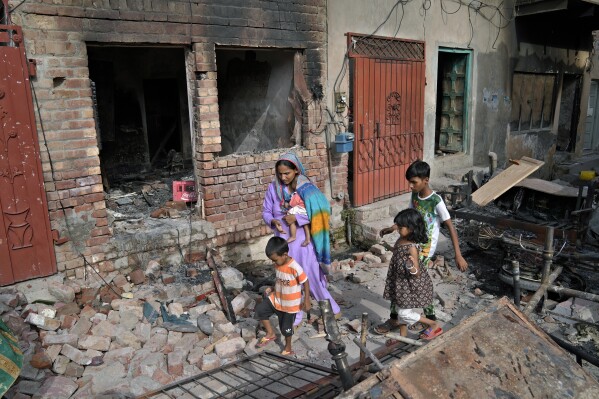 A Christian woman with her children walk through the rubble of homes vandalized by angry Muslim mob in Jaranwala near Faisalabad, Pakistan, Thursday, Aug. 17, 2023. Muslims in eastern Pakistan went on a rampage Wednesday over allegations that a Christian man had desecrated the Quran, demolishing the man's house, burning churches and damaging several other homes, police and local Christians said. (AP Photo/K.M. Chaudary)