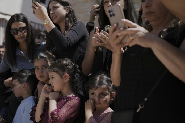 Children look on with emotion while adults capture the moment on their phones during a Good Friday reenactment outside the Maronite Church of St. George in Quraye, near the southern port city of Sidon, Lebanon, Friday, April 18, 2025. (AP Photo/Hassan Ammar)