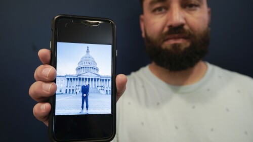 Mohammad Ahmadi poses for a portrait in Alexandria, Va., Friday, July 7, 2023, while holding a phone showing a digital photograph of his relative Nasrat Ahmad Yar who was shot and killed on July 3, in Washington, while working as a ride-share driver. Ahmad Yar was an Afghan immigrant who'd worked as an interpreter for the U.S. military in Afghanistan. (AP Photo/Serkan Gurbuz)