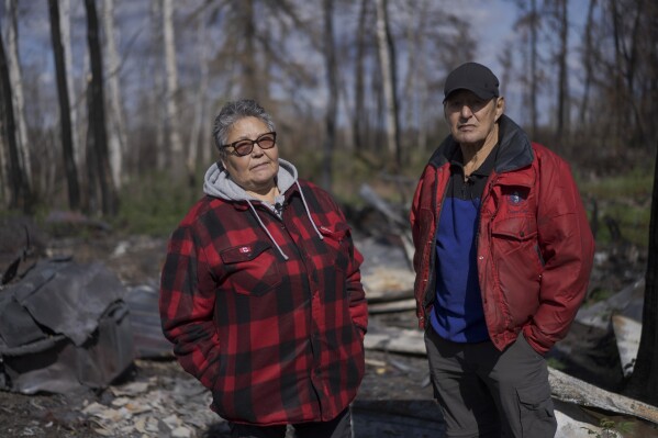 Julia Cardinal, left, and her husband Happy Cardinal stand for a portrait near what remains of his cabin, destroyed by wildfires, near Fort Chipewyan, Canada, on Sunday, Sep. 3, 2023. (AP Photo/Victor R. Caivano)