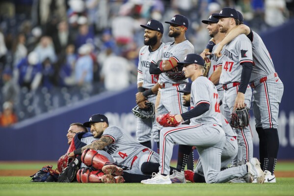 Minnesota Twins catcher Christian Vazquez (8) and shortstop Carlos Correa (4) lie in front of the team as players pose for a photo to celebrate their win against the Toronto Blue Jays in a baseball game Friday, May 10, 2024, in Toronto. (Cole Burtson/The Canadian Press via AP)