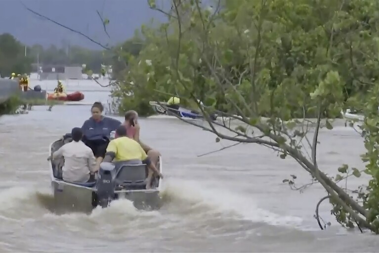In this image from a video, people ride in boats in flooded river in Cairns, Australia Monday, Dec. 18, 2023. More than 300 people were rescued overnight from floodwaters in northeast Australia, with dozens of residents clinging to roofs, officials said on Monday. (Australian Broadcasting Corp. via AP)