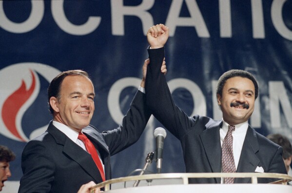 Outgoing Democratic National Committee chairman Paul Kirk Jr., left, holds up the hand of Ron Brown, the new chairman, after his appointment to the post in Washington, Feb. 10, 1989. (APPhoto/Barry Thumma)