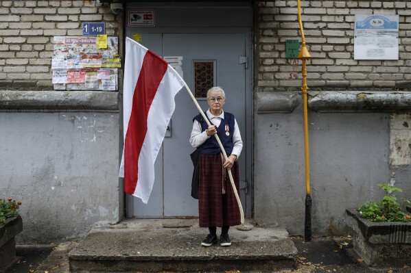 Nina Bahinskaya, 73, poses for a photo holding a flag that became the symbole of the opposition at an entrance of her apartment building in Minsk, Belarus, on Sept. 10, 2020. (AP Photo, File)