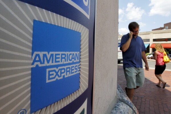 FILE - People walk past an American Express logo near the entrance to a bank in the Harvard Square neighborhood of Cambridge, Mass., Tuesday, July 19, 2011. American Express on Monday, Oct. 16, 2023, announced a multi-year partnership with Formula One in the first new sports sponsorship in more than a decade for the global payment company. The (AP Photo/Steven Senne, File)