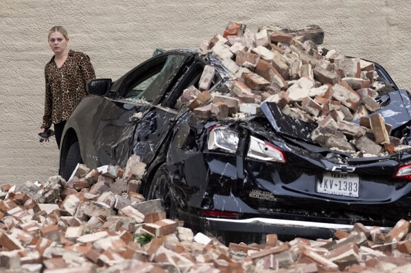 A woman looks at the damage caused by fallen bricks from a building wall in the aftermath of a severe thunderstorm Friday, May 17, 2024, in Houston. (AP Photo/David J. Phillip)
