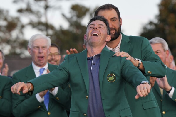 Scottie Scheffler puts the green Jacket on winner, Rory McIlroy, of Northern Ireland, at the Masters golf tournament, Sunday, April 13, 2025, in Augusta, Ga. (AP Photo/David J. Phillip)