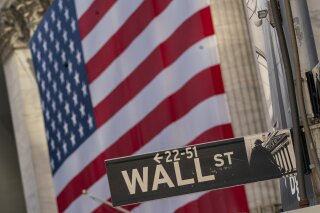 The Wall Street street sign is framed by a giant American flag hanging on the New York Stock Exchange, in a Monday, Sept. 21, 2020 file photo. Stocks are opening higher on Wall Street, recovering after their first four-week losing streak in more than a year. A burst of corporate deals helped give investors confidence to put money back in the market, and the S&P 500 rose 1.4% in the early going Monday, Sept. 28, 2020. (AP Photo/Mary Altaffer, File)