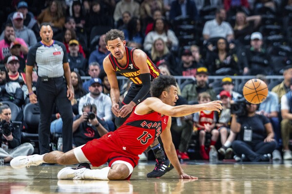 Toronto Raptors forward Jordan Nwora (13) passes the ball after falling next to Atlanta Hawks' Trae Young during the first half of an NBA basketball game Friday, Feb. 23, 2024, in Atlanta. (AP Photo/Jason Allen)