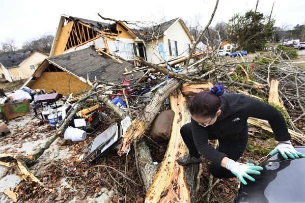 A resident climbs over debris after her friend's home in Clarksville, Tennessee, was lifted off its foundation on Sunday, Dec. 10, 2023. Tornadoes caused catastrophic damage in the central part of Tennessee on Saturday. (AP Photo/Mark Zaleski)