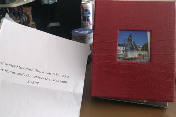 A photo album, that had been recently stolen from the Massachusetts bar made famous in Sebastian Junger's 1997 book "The Perfect Storm" and the 2000 movie of the same name, sits at a table along with a note of apology after it was returned, Wednesday, June 23, 2021, in Gloucester, Mass. The album, which contained irreplaceable pictures of regulars — some deceased — along with George Clooney, Mark Wahlberg and other stars of the Oscar-nominated movie was kept under the bar, but always made available to curious patrons who wanted to take a look. (Sean Horgan/ Gloucester Daily Times via AP)