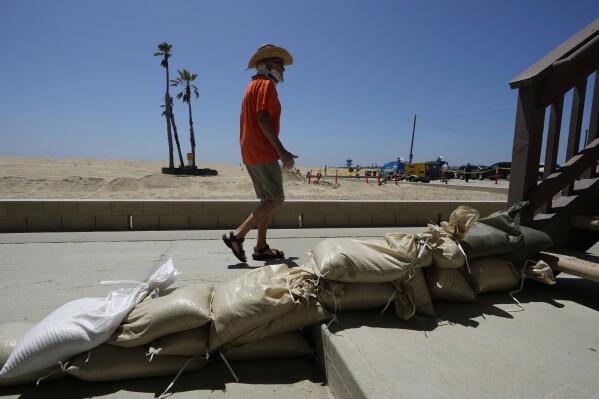 Seal Beach resident Tom Ostrom walks past a home protected with sandbags in Seal Beach, Calif., Friday, Aug. 18, 2023, as residents prepare for an approaching storm. (AP Photo/Damian Dovarganes)