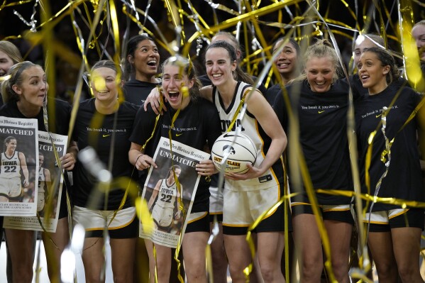 Iowa guard Caitlin Clark (22) stands with teammate after being presented with a commemorative basketball after the team's NCAA college basketball game against Michigan, Thursday, Feb. 15, 2024, in Iowa City, Iowa. Clark broke the NCAA women's career scoring record. (AP Photo/Matthew Putney)