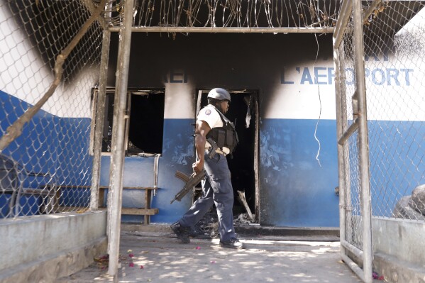 A police officer walks at a police station set on fire by armed gangs in Port-au-Prince, Haiti, Tuesday, March 5, 2024. Prime Minister Ariel Henry has been absent since the country's latest and most serious outbreak of violence started the previous week, and armed groups have seized on the power void. (AP Photo/Odelyn Joseph)
