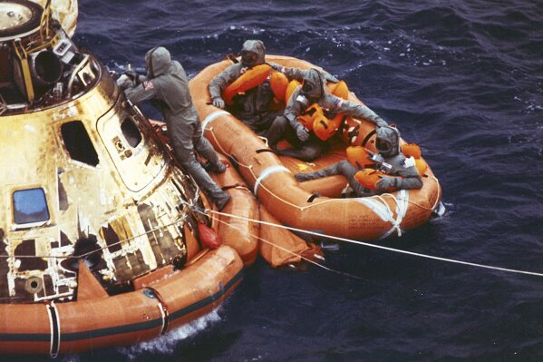 FILE - In this July 24, 1969, file photo from the U.S. Navy, Lt. Clancy Hatleberg closes the Apollo 11 spacecraft hatch as astronauts Neil Armstrong, Michael Collins, and Buzz Aldrin, Jr., await helicopter pickup from their life raft after splashdown in the Pacific Ocean, 900 miles southwest of Hawaii, returning to Earth from a successful lunar landing mission. Hatleberg's mission was to decontaminate the astronauts and their command module, Columbia, immediately following splashdown. The astronauts' trip to the moon concluded with a stay in Hawaii. July 20 marked the 50th anniversary of the moon landing, but after those historic first steps NASA still had to get the three astronauts safely back to Earth - and the waters off Hawaii are where the cone-shaped spacecraft splashed down. (Milt Putnam/U.S. Navy via AP, File)