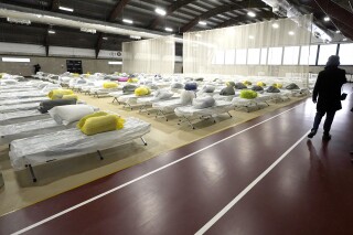 FILE - A passer-by walks through a portion of the Cass Recreational Complex which has been turned into a temporary shelter site for families experiencing homelessness, Jan. 31, 2024, in Boston. Massachusetts will begin limiting how long homeless families can stay in shelters as the state continues to grapple with an influx of homeless migrants. (AP Photo/Steven Senne, File)