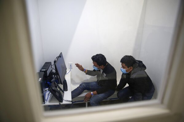 Migrants speak to their relatives inside a phone booth after being processed at the intake area of the U.S. Customs and Border Protection facility, the main detention center for unaccompanied children in the Rio Grande Valley, in Donna, Texas, Tuesday, March 30, 2021.  (AP Photo/Dario Lopez-Mills, Pool)
