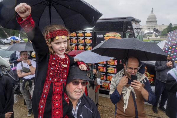 Una niña de 7 años de Springfield, Virginia, que viste un atuendo tradicional, levanta el puño en brazos de su abuelo, de origen palestino, en una manifestación propalestina, el sábado 18 de mayo de 2024, en el National Mall, cerca del Capitolio, en Washington. (AP Foto/Jacquelyn Martin)