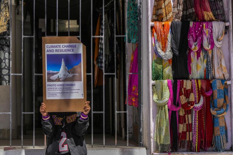 A young climate activist holds a placard to advertise a local photo exhibition on climate change in the main business center of Leh town in the cold desert region of Ladakh, India, Monday, Sept.19, 2022. In the remote Himalayan region, glaciers are melting fast while still villagers largely depend on glacial runoff for water. (AP Photo/Mukhtar Khan)