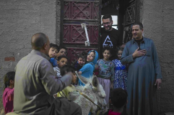Neighbours greet 55-year-old "musaharati," or "dawn caller" Essam Sayed, as he rides his donkey to wake people up for a meal before sunrise, during the Islamic holy month of Ramadan, in the Arab Ghoneim district of Helwan on the southern outskirts of Cairo, Egypt, Saturday, March 15, 2025.(AP Photo/Amr Nabil)