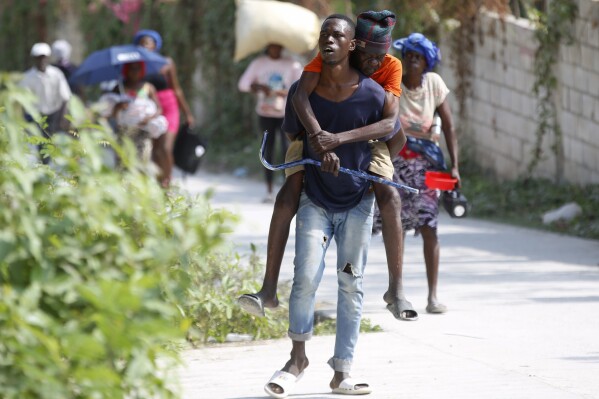 Un residente carga en su espalda a un anciano mientras huyen de su vivienda para evitar los enfrentamientos entre grupos armados, el miércoles 31 de enero de 2024, en el distrito de Petion-Ville, Haití. (AP Foto/Odelyn Joseph)