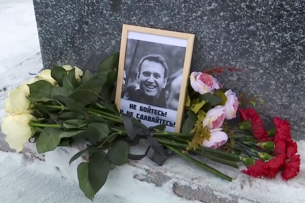 This grab taken from video shows flowers and a portrait of Russian opposition leader Alexei Navalny that Lyudmila Navalnaya, mother of Russian opposition leader Alexei Navalny, put to pay tribute to her son at the at the memorial to victims of political repression, in Salekhard, 1937 km (1211 miles) northeast of Moscow, Russia, on Tuesday, Feb. 20, 2024. Russians across the vast country streamed to ad-hoc memorials with flowers and candles to pay tribute to Alexei Navalny, the most famous Russian opposition leader and the Kremlin's fiercest critic. Russian officials reported that Navalny, 47, died in prison on Friday. (AP Photo)