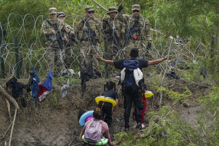 FILE - A migrant gestures to Texas National Guards standing behind razor wire on the bank of the Rio Grande river, seen from Matamoros, Mexico, May 11, 2023. (AP Photo/Fernando Llano, File)